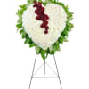 Heart-shaped standing spray of white flowers with a red rose cascade on a metal easel.