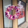Large pink and purple flower wreath on a wooden easel displayed outside a storefront