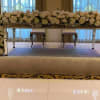 Long mirrored table wrapped in dense white and blush floral garlands on a stage.