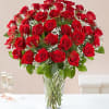 Tall clear vase filled with many red roses and white filler flowers on a white table