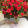 Tall arrangement of red roses, carnations, and lilies in a clear glass vase