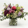 Mixed bouquet of pink, purple, and green flowers in a square glass vase