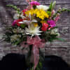 Mixed bouquet of pink, white, and yellow flowers in a glass vase with a pink ribbon.