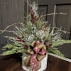 Holiday arrangement with evergreen branches, red berries, and a decorative bow in a round container