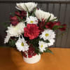 Red and white mixed flower arrangement in a white holiday container