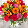 Mixed bouquet of roses, lilies, gerbera daisies, and carnations in a glass vase