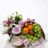 Basket arrangement with lilies, roses, and fruit topped with a pink ribbon