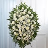 Large white funeral spray with mixed blooms and palm leaves on an easel
