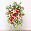 Standing floral spray with pink and red roses, white daisies, and tropical leaves