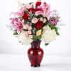 Bouquet of pink lilies, red roses, and white hydrangeas in a red glass vase
