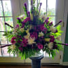 Large purple and white floral arrangement in a pedestal vase