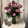 Pink roses arranged in a glass vase with two purple candles beside it
