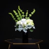 White orchids and pale hydrangeas in a black vase with tall green spikes