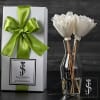 White flowers in a clear vase beside a gift box with a green ribbon