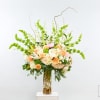 Tall floral arrangement in a clear glass vase with peach, white, and pink blooms