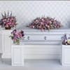 Purple and pink floral funeral casket spray with matching standing arrangements