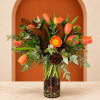 Orange tulips arranged in a glass vase with pinecones and greenery.