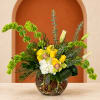 Yellow roses and white orchids in a glass bowl vase with greenery