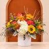 Autumn floral arrangement in a white vase with roses, sunflowers, and a pumpkin accent.