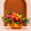 Orange and purple floral arrangement in a pumpkin-shaped container