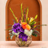 Colorful floral arrangement in a round glass vase with purple orchids and orange roses