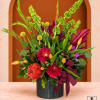 Tropical floral arrangement in a black vase with a burgundy ribbon