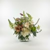 Mixed floral arrangement in a clear glass vase with cream, green, and purple blooms