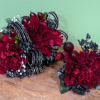 Two red floral arrangements with dark ribbon and berry accents on a table