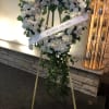 White floral standing wreath on an easel with a memorial ribbon