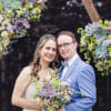 Bride and groom holding a bouquet in front of a floral arch