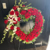 Heart-shaped red floral wreath on a stand with white lilies and roses