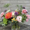 Mixed bouquet of pink, orange, purple, and white flowers in a glass vase