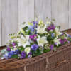 White lilies and purple-blue flowers arranged in a wicker casket spray