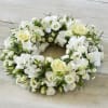 White floral wreath with roses and small blooms on a wood surface