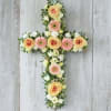 Floral cross arrangement with peach roses and pink daisies on a white wood background