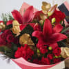 Red lilies and roses arranged with gold accents in pink wrapping