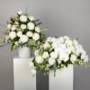 Two white floral arrangements in white pedestal vases
