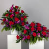 Two red rose arrangements with purple accents in white containers