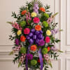 Standing floral spray with a purple ribbon bow and mixed blooms