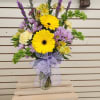 Bouquet of yellow gerbera daisies and purple flowers in a glass vase with a lavender bow