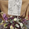 Memorial plaque with angel relief above a purple and white floral arrangement