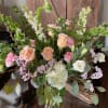 Tall arrangement of peach roses, white hydrangea, pink flowers and green bells of Ireland in a glass vase