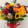 Mixed bouquet of roses, gerbera daisies, and sunflowers in a glass vase with a red ribbon
