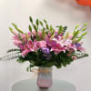 Pink lilies and purple flowers in a frosted vase with a bow