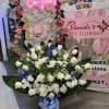 Large white rose arrangement in a white container with blue ribbon