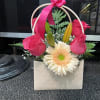 Pink roses and a cream gerbera daisy in a gift bag with a ribbon handle