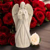 White angel figurine in front of red roses with a cream rose at the base