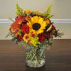Mixed bouquet of sunflowers, red roses, and autumn flowers in a glass vase
