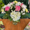 Pink roses and white daisies arranged in a glass vase with blue hydrangea