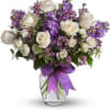 White roses and purple flowers arranged in a glass vase with a purple ribbon
